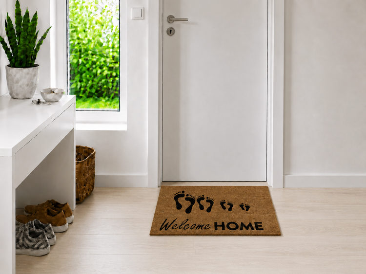 Fußmatte mit Welcome Home Schriftzug und Fußabdrücken vor einer weißen Tür im Eingangsbereich.