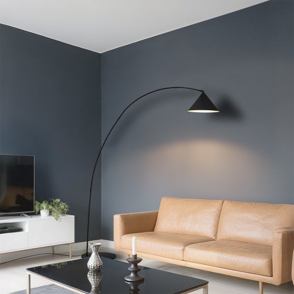 Schwarze Bogenlampe im modernen Wohnzimmer über einem hellbraunen Ledersofa vor grauen Wänden.