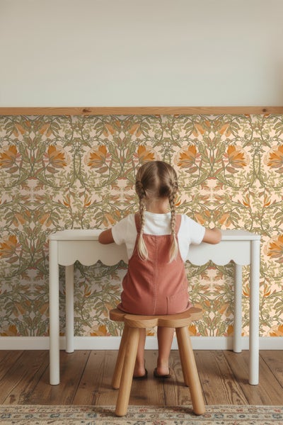 Kind sitzt an einem Schreibtisch vor einer floralen Tapete.