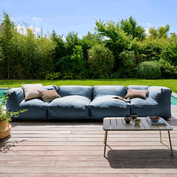 Modernes 4-Sitzer Gartensofa aus blauem Stoff auf einer Holzterrasse mit einem Loungetisch im Garten vor grünem Hintergrund.