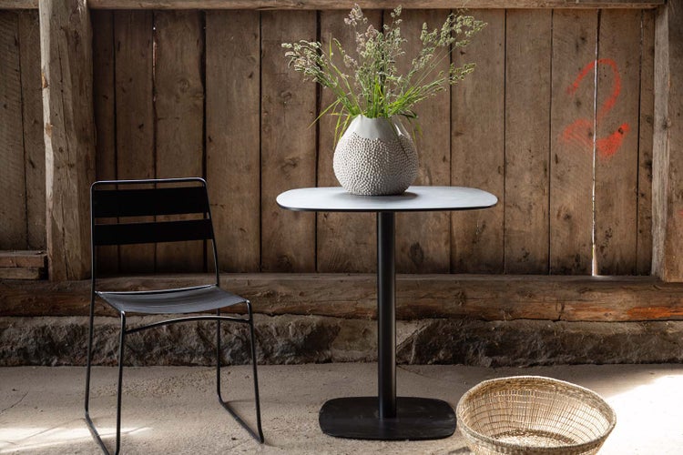 Szene mit einem Tisch, einer Vase mit Blumen, einem Stuhl und einem Korb vor einer Holzwand