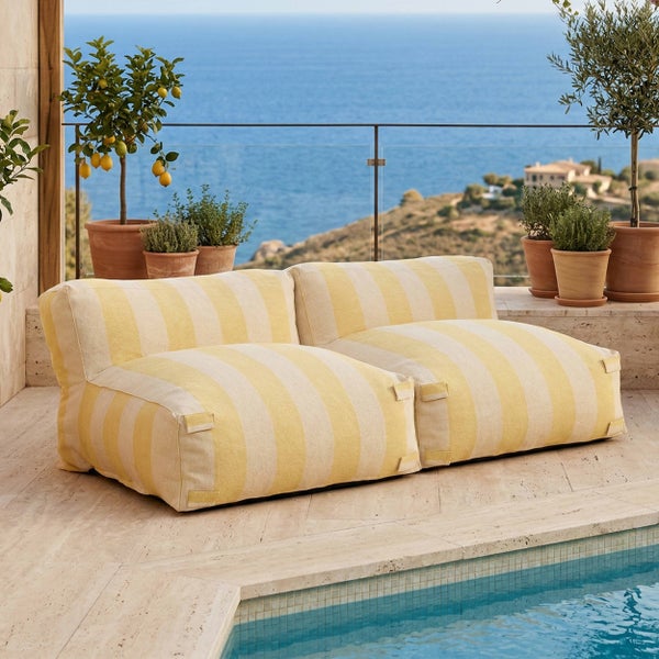Gestreiftes Outdoor-Sitzsack-Sofa in Gelb und Weiß auf einer Steinterrasse am Pool mit Meerblick und Zitronenbaum.
