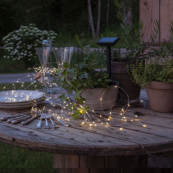 Dekorativer Gartentisch mit Geschirr, Besteck, Solarleuchte und Lichterkette