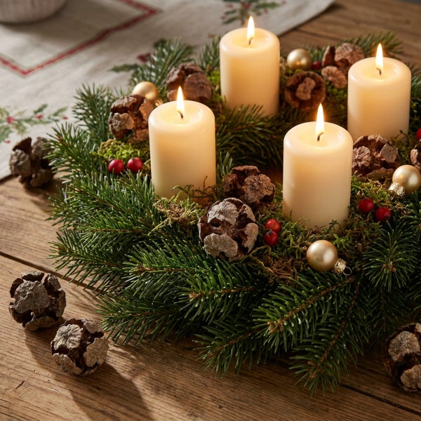 Adventskranz mit vier brennenden Stumpenkerzen geschmückt mit Tannenzweigen Tannenzapfen und Weihnachtskugeln auf einem Holztisch