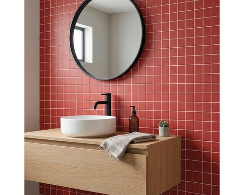 Modernes Badezimmer mit roten quadratischen Mosaikfliesen an der Wand, weißem Aufsatzwaschbecken auf Holzunterschrank und rundem Spiegel.