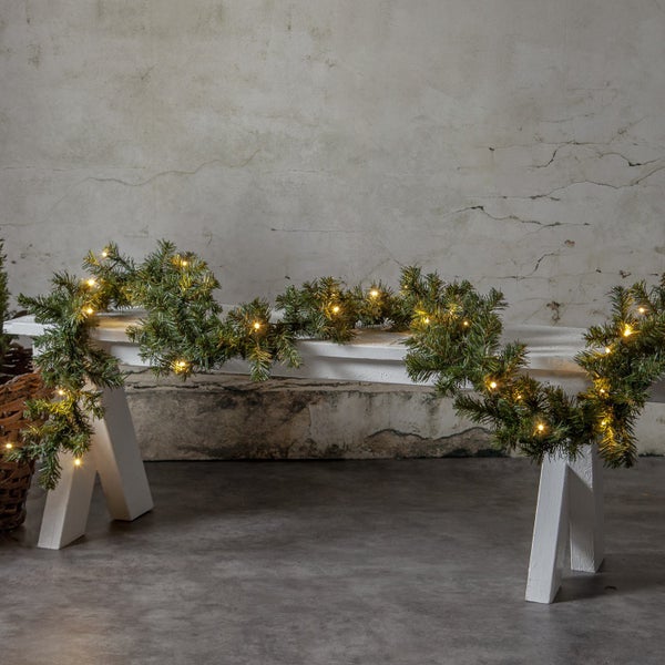Dekorativer Tannenkranz mit Beleuchtung auf einer weißen Bank