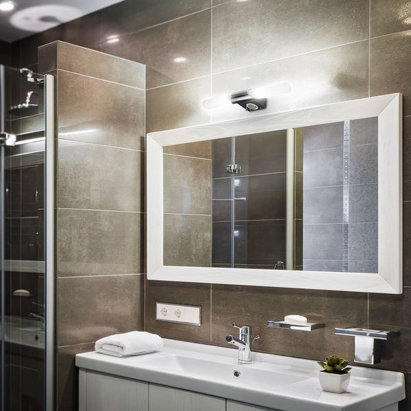 Modernes Badezimmer mit LED-Wandleuchte über Spiegel mit weißem Rahmen, Waschbecken mit Chromarmatur und Fliesen in Natursteinoptik.