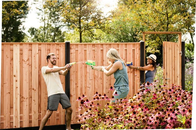 Sichtschutzzaun aus hellem Holz mit schwarzen Pfosten und passendem Gartentor in einem sonnigen Garten mit blühenden Blumen.