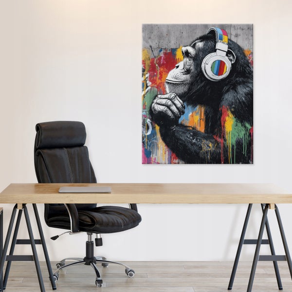 Wandbild eines Schimpansen mit Kopfhörern im Street Art Stil über einem modernen Schreibtisch mit schwarzem Bürostuhl.