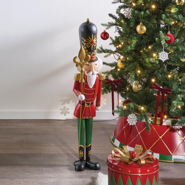 Große Nussknacker Weihnachtsfigur als Dekoration stehend neben einem geschmückten Weihnachtsbaum mit Weihnachtsgeschenk.