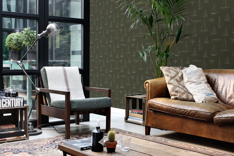 Vliestapete mit Segelschiff-Muster in einem Wohnzimmer mit Ledersofa, Holzsesseln und Zimmerpflanze im industriellen Stil.