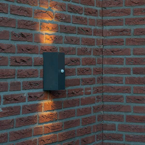Rechteckige Außenwandleuchte mit Bewegungsmelder an einer Backsteinwand, Lichtstrahl nach oben und unten.
