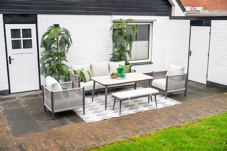 Moderne Garten-Lounge-Gruppe aus Aluminium und Seilgeflecht mit Sofa, Sesseln, Esstisch und Bank auf einer gepflasterten Terrasse.