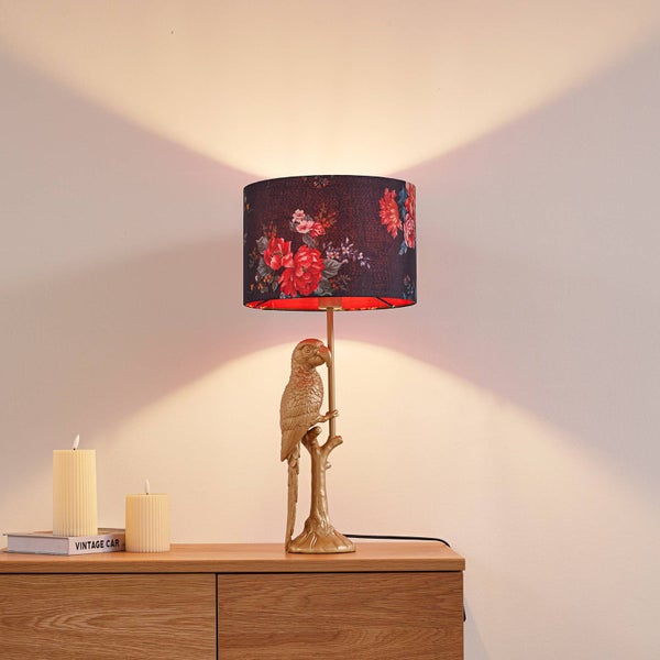 Dekorative Tischleuchte mit Papageienfuß und floralem Schirm auf einem Holzschrank