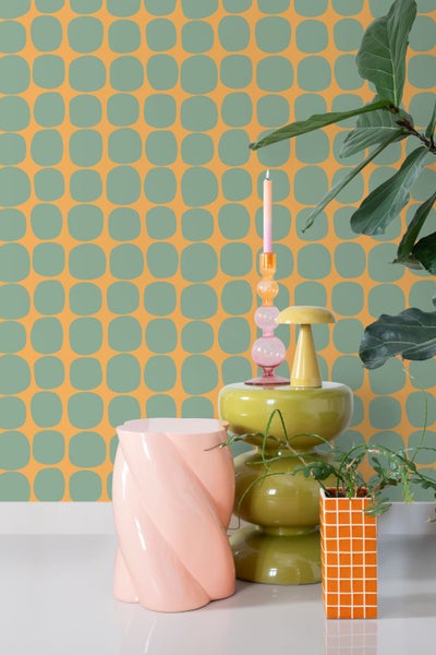 Vliestapete mit geometrischem Muster aus abgerundeten Quadraten in einem modernen Raum mit dekorativem Beistelltisch, Kerzenständer und Zimmerpflanzen.