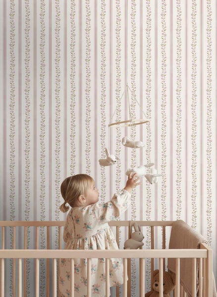 Tapete mit vertikalem Streifenmuster und floralen Ranken in einem hellen Kinderzimmer mit Kind im Gitterbett.
