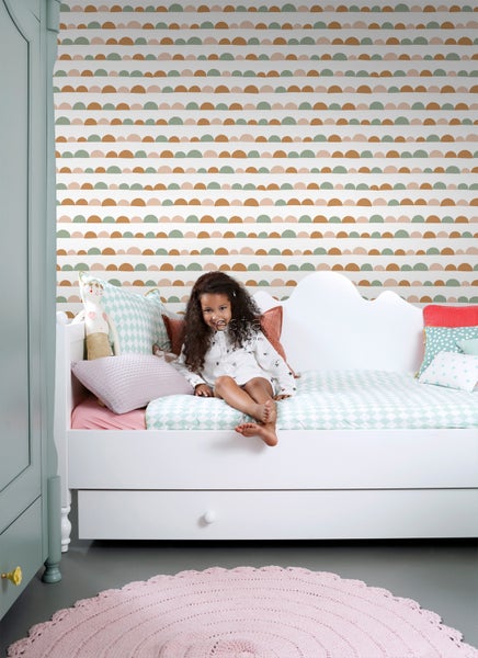 Kinderzimmer mit Mädchen auf einem weißen Bett vor einer Tapete mit Halbkreis-Muster