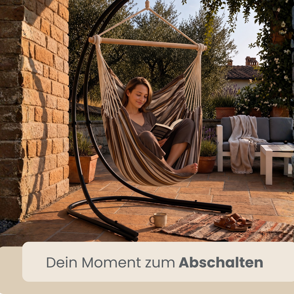 Frau liest in einem hängenden Hängesessel mit Gestell auf einer Terrasse