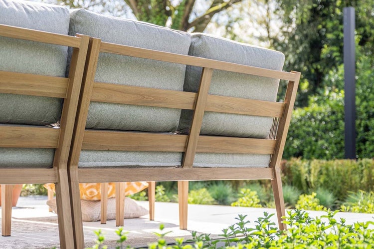 Rückansicht eines Gartensofas aus Holz mit hellgrauen Polstern auf einer sonnigen Terrasse im Garten.