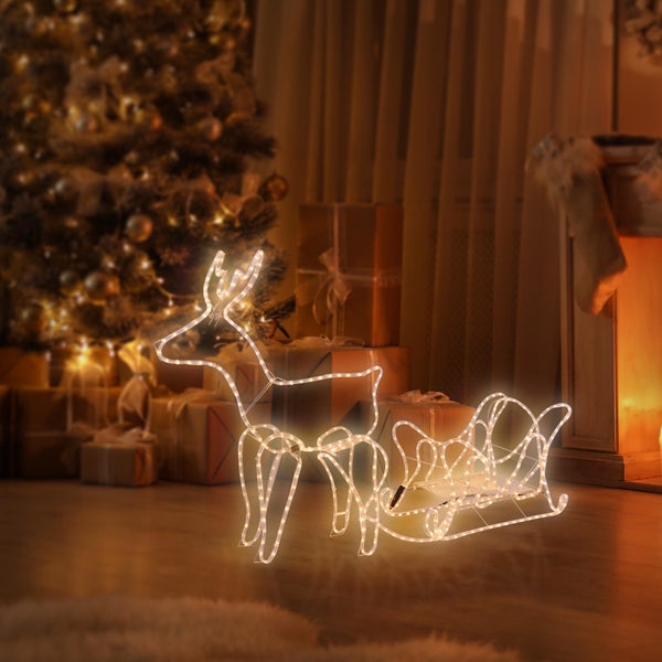 Beleuchtete LED Figur Rentier mit Schlitten als Weihnachtsdekoration für den Innenbereich in wohnlicher Umgebung mit Weihnachtsbaum und Geschenken