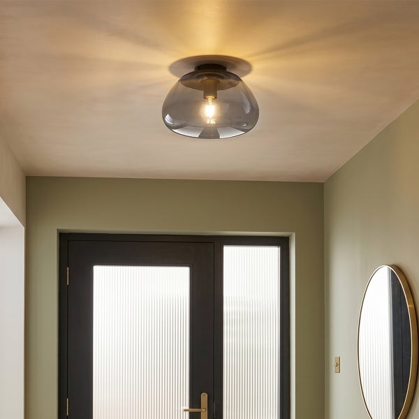 Moderne Deckenleuchte mit gläsernem Lampenschirm in einem Flur mit einer dunklen Tür und einem runden Wandspiegel.