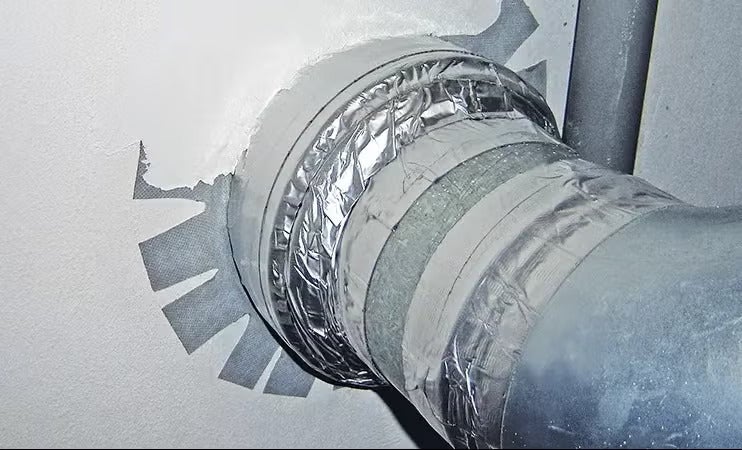 Ein metallisches Lüftungsrohr ist mit Klebeband an einer Wand luftdicht montiert und fixiert.