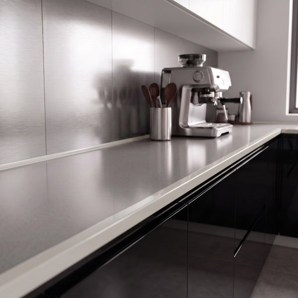 Moderne Küche mit glänzenden Fronten, Metallrückwand und Espressomaschine auf einer Arbeitsplatte in einer aufgeräumten, hellen Küchenumgebung.