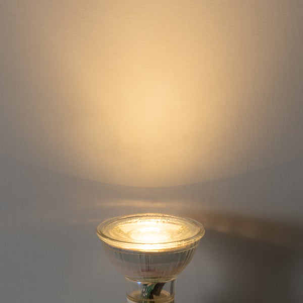 Eingeschaltetes LED-Leuchtmittel mit warmweißem Lichtkegel an einer Wand.