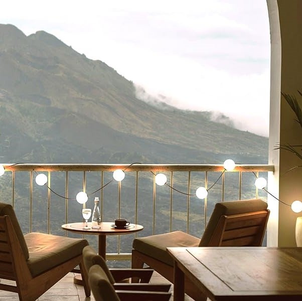 Szene mit Lichterkette, Tisch und Stühlen auf einem Balkon mit Bergblick