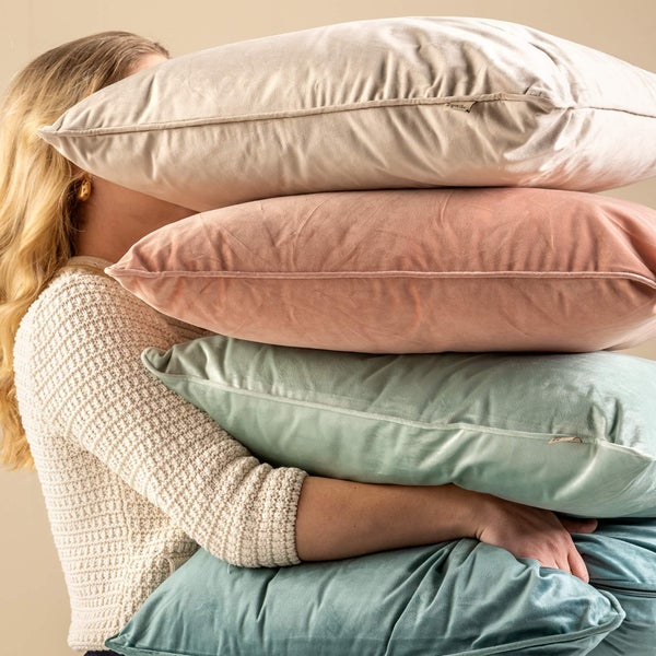 Person im Strickpullover hält vier dekorative Kissen aus Samt.