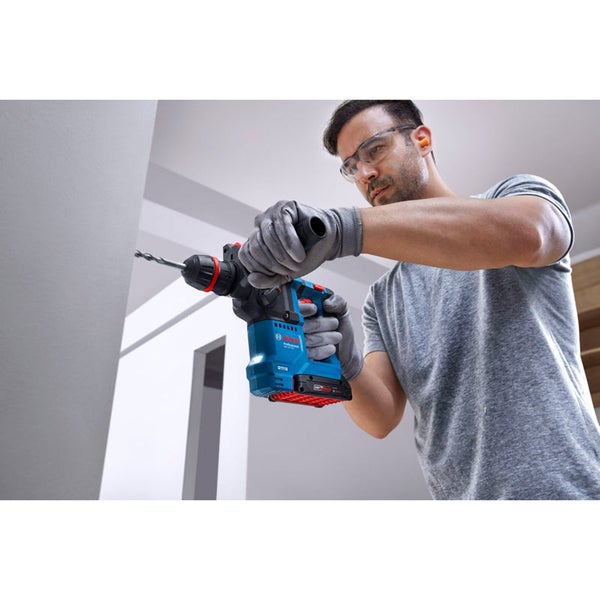 Handwerker bohrt mit einem Bosch Professional Akku Bohrhammer in eine Wand und trägt Schutzausrüstung wie Handschuhe und Schutzbrille.