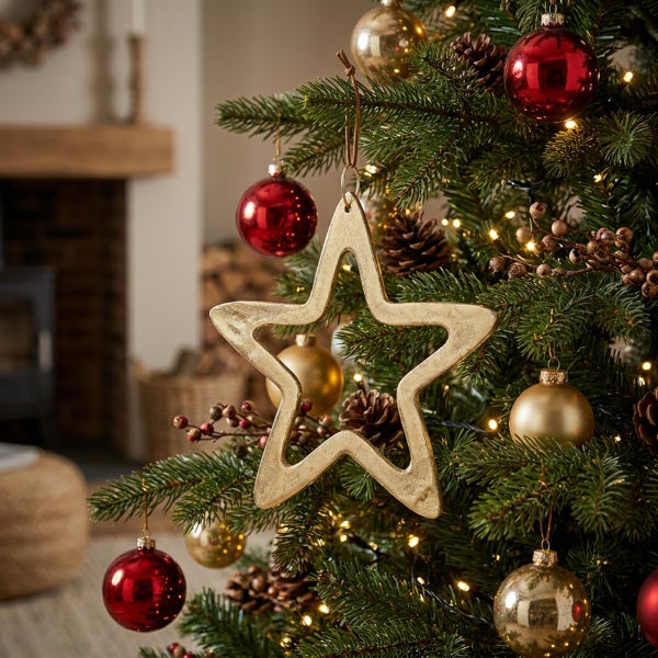 Weihnachtsbaum mit goldenem Sternanhänger und Dekokugeln in einer gemütlich dekorierten Wohnumgebung mit Kamin.
