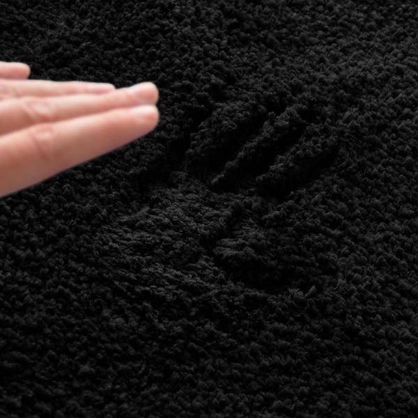 Detailaufnahme eines schwarzen, flauschigen Teppichs mit Handabdruck