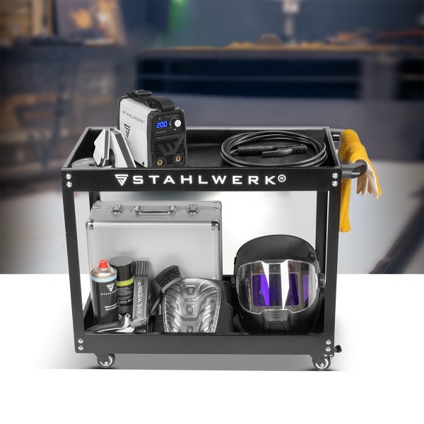 Schwarzer STAHLWERK Schweißwagen mit zwei Ablagen, bestückt mit Schweißgerät, Schweißhelm, Werkzeugkoffer und Zubehör in einer Werkstatt.