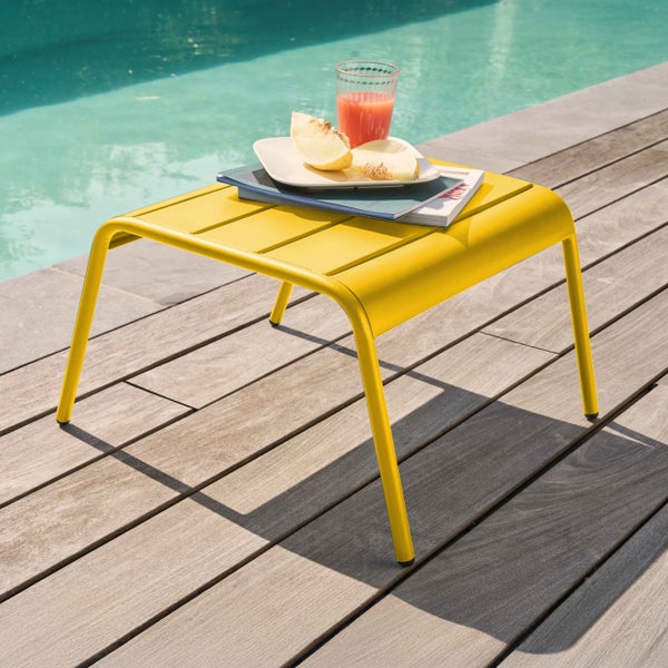 Gelber Beistelltisch aus Metall mit Lamellenoberfläche auf einer Holzterrasse am Pool.