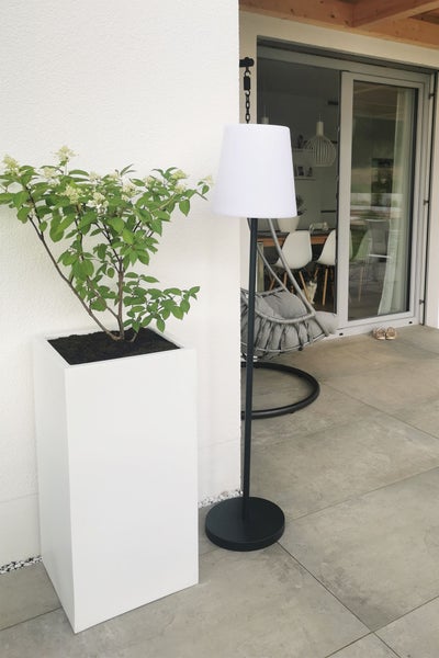 Moderne Terrasse mit weißem Pflanzkübel und schwarzer Außenstehleuchte mit weißem Schirm.