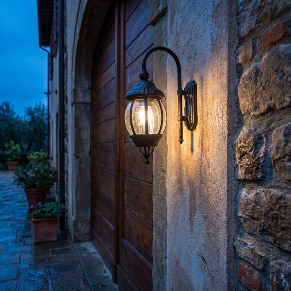 Klassische Außenwandleuchte in Laternenform an einer Steinwand neben einer Holztür, warmes Licht, rustikaler Stil.