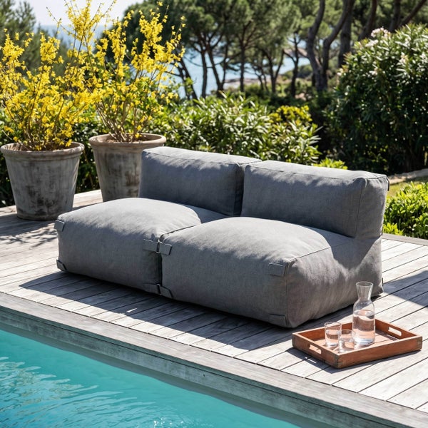 Graues modulares Outdoor Loungesofa auf einer Holzterrasse am Pool, umgeben von Pflanzen im Garten.