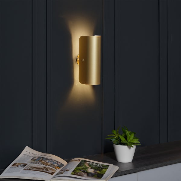 Goldene Wandleuchte neben einer Zeitschrift und einer Topfpflanze