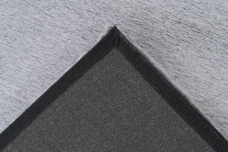 Nahaufnahme der Ecke eines grauen Teppichs mit weichem Flor und gewebter Unterseite.