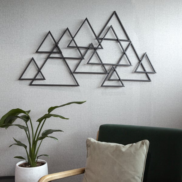 Wanddekoration aus Metall mit überlappenden Dreiecken in einem modernen Wohnzimmer mit Zimmerpflanze und Sessel.
