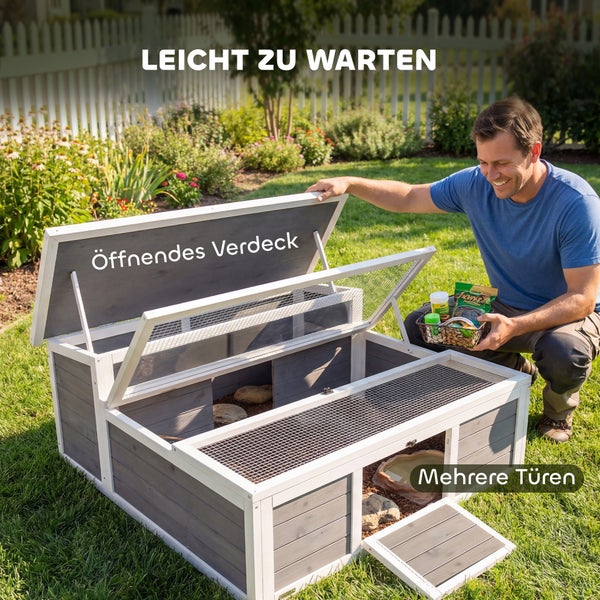 Schildkrötenhaus aus grauem Holz mit weißem Rahmen, aufklappbarem Dach und Gittertüren, in einem Garten mit einer Person bei der Pflege.