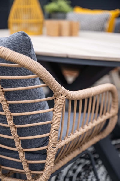 Detail eines Gartenstuhls mit Geflechtstruktur und Sitzkissen an einem Tisch.