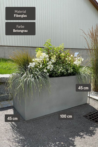 Rechteckiger Pflanztrog aus Fiberglas in Betongrau, 100 mal 45 mal 45 Zentimeter, bepflanzt mit weißen Blumen und Ziergräsern im Freien.