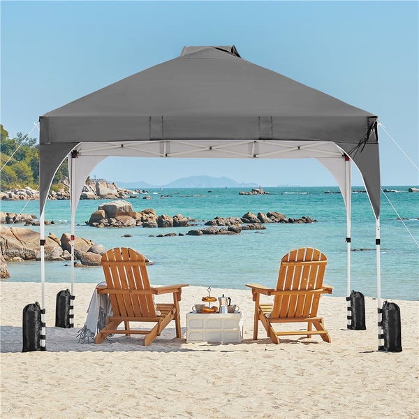 Grauer Pavillon mit zwei Holzstühlen und kleinem Tisch am Strand.