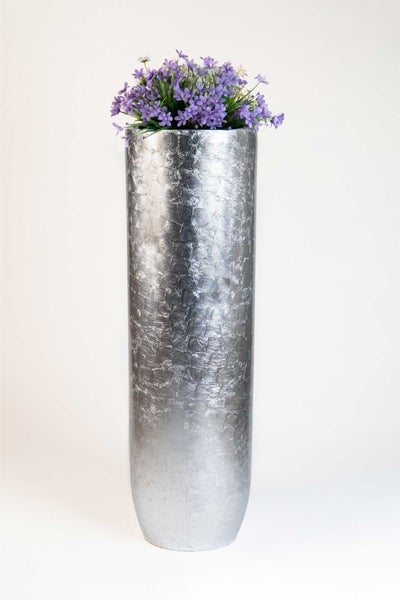 Hohe Bodenvase mit strukturierter, silberfarbener Oberfläche und lila Kunstblumen.