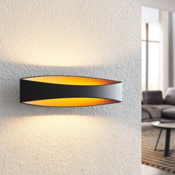 Moderne ovale Wandleuchte in Schwarz und Gold mit Lichtaustritt nach oben und unten an einer strukturierten Wand in einem Wohnzimmer.