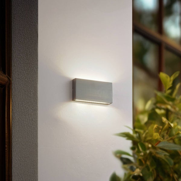 Moderne rechteckige Außenwandleuchte aus gebürstetem Metall mit Up-and-Down-Lichteffekt an einer weißen Hauswand montiert.