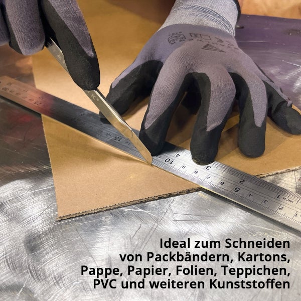 Cuttermesser schneidet Pappe an einem Metalllineal auf einer Werkbank, Hand mit Schutzhandschuh.