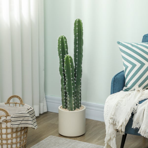 Künstlicher Kaktus mit drei Säulen in einem weißen Topf, platziert in einem hellen Wohnzimmer neben einem blauen Sessel und einem Weidenkorb.